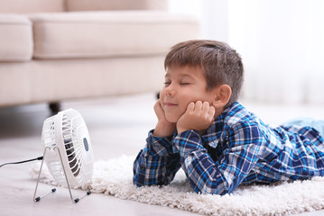 Naklejka premium Little boy refreshing from heat in front of small fan at home