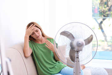 Fototapeta premium Woman suffering from heat in front of fan at home