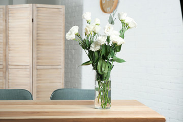 Vase with beautiful flowers as element of interior design on table in room. Space for text