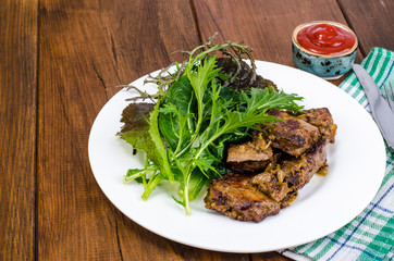 Slices of fried liver, green leaves of salads