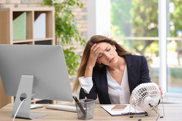 Businesswoman suffering from heat in front of small fan at workplace