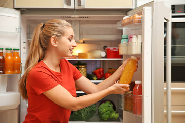 Young woman with juice near refrigerator at home
