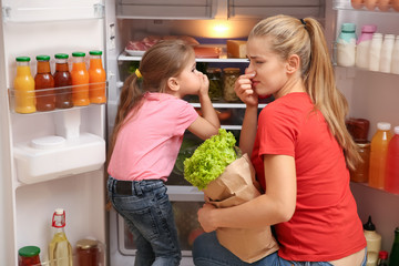 Young mother and daughter holding noses cause of bad smell from refrigerator at home - obrazy, fototapety, plakaty