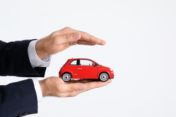 Male insurance agent holding toy car on white background, closeup. Space for text