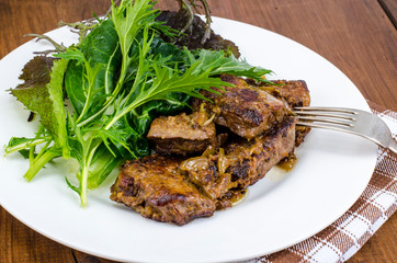 Slices of fried liver, green leaves of salads
