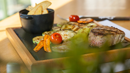 Beef steak served with baked potatoes and vegetables on a wooden plate in restourant.