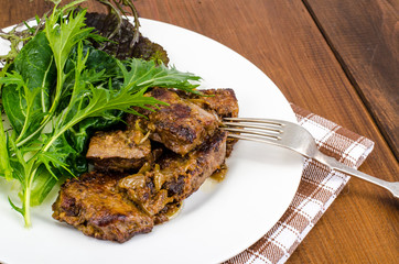 Slices of fried liver, green leaves of salads