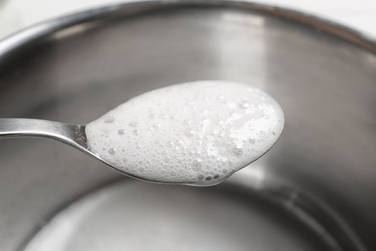 Chemical reaction of vinegar and baking soda in spoon over saucepan, closeup