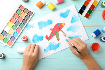 Girl painting picture of airplane on table, top view