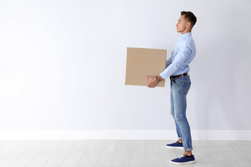 Full length portrait of young man carrying heavy cardboard box near white wall. Posture concept