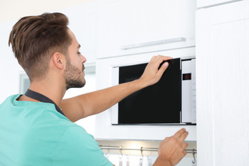 Young man using modern microwave oven at home