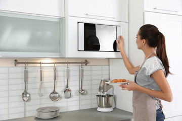 Young woman with plate of croissants near microwave oven in kitchen