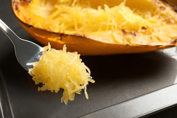 Fork with flesh of cooked spaghetti squash on blurred background, closeup