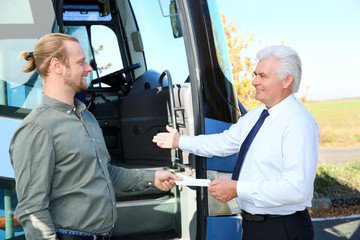 Professional driver taking ticket from passenger near bus