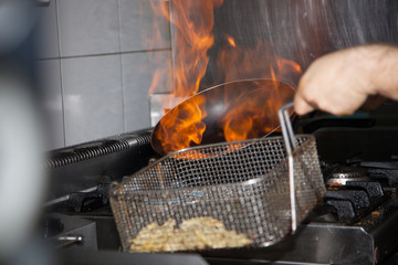 Chef Cooking With Fire In Frying Pan. Professional chef in a commercial kitchen cooking flambe style. Chef frying food in flaming pan on gas hob in commercial kitchen