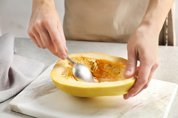 Woman scraping flesh of spaghetti squash with spoon on table, closeup