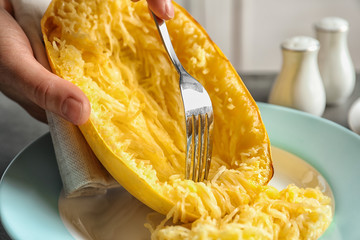 Woman scraping flesh of cooked spaghetti squash with fork on table, closeup