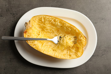 Plate with cooked spaghetti squash and fork on gray background
