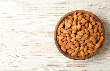 Tasty organic almond nuts in bowl and space for text on table, top view