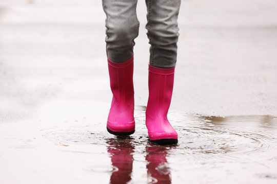 Little girl wearing rubber boots splashing in puddle on rainy day, focus of legs. Autumn walk