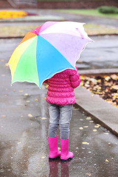 Little girl with umbrella taking autumn walk in city on rainy day