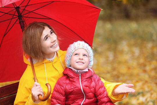 Mother and daughter with umbrella in autumn park on rainy day