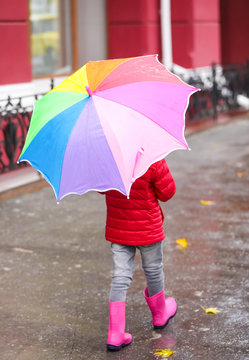 Little girl with umbrella taking autumn walk in city on rainy day