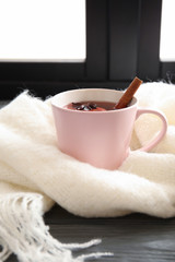 Cup of hot winter drink with knitted scarf near window. Cozy season
