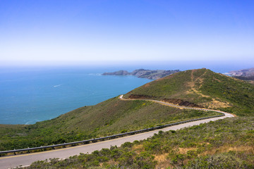 Beautiful views of the green hills of Marin Headlands crossed by a winding road; the Pacific Ocean coastline in the background; north San Francisco bay area, California