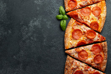 Cut into slices delicious fresh pizza with sausage pepperoni and cheese on a dark background. Top view with copy space for text. Pizza on the black concrete table. flat lay - obrazy, fototapety, plakaty
