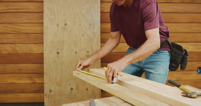 Skilled carpenter carefully measures and marks lengths on wood