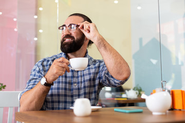 Coffee break. Successful bearded pleasant businessman wearing glasses having coffee break in cafeteria