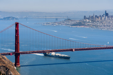 Cargo ship passing under Golden Gate Bridge on a sunny day; San Francisco skyline in the...