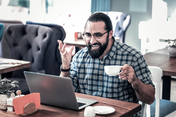 Happy freelancer. Dark-haired freelancer wearing glasses feeling happy after getting his work approved