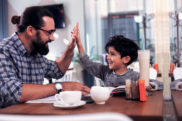 Beaming son. Cute beaming son giving high five his father after studying foreign language together