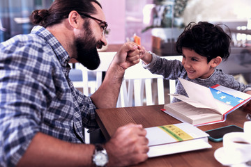 Have fun. Cheerful cute dark-eyed son feeling amazing having fun with his caring loving father