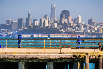 People fishing from one of the piers facing the San Francisco downtown; the city's financial district skyline visible in the background; California