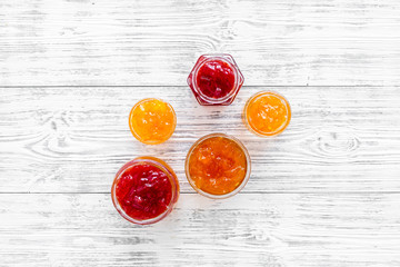 Set of sweet jams in glass jars on white wooden background top view space for text