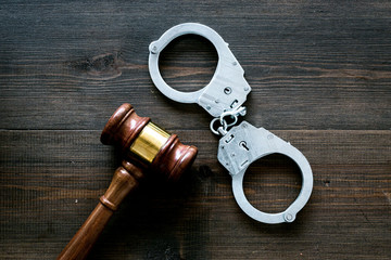 Arrest concept. Metal handcuffs near judge gavel on dark wooden background top view