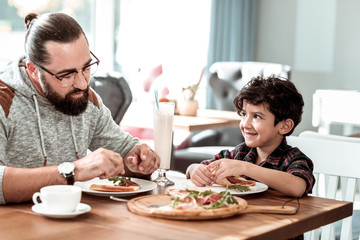 Fototapeta na wymiar Yummy pizza. Bearded father and cute son eating extremely yummy pizza with bacon and cheese