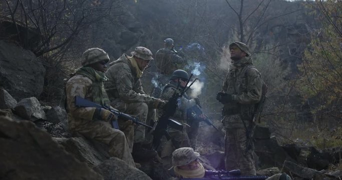 Medium slow motion shot of soldiers taking a break from patrol and smoking while on a mission