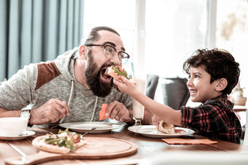 High five. Emotional modern father giving high five his funny little son while eating pizza together