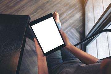 Mockup image of a woman sitting and holding black tablet pc with blank white desktop screen