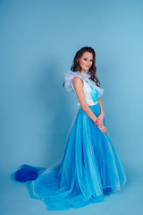 Fototapeta na wymiar Young beauty woman in tulle fluttering blue dress.Beautiful girl with make-up , hairstyle and gorgeous look.female model prom seamstress and designer clothes tailor on a blue background in the studio