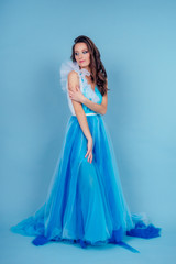 Fototapeta na wymiar Young beauty woman in tulle fluttering blue dress.Beautiful girl with make-up , hairstyle and gorgeous look.female model prom seamstress and designer clothes tailor on a blue background in the studio
