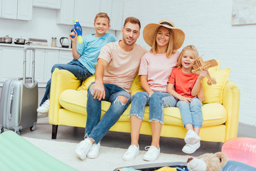 happy family looking at camera and resting on sofa after packing for summer vacation, travel concept