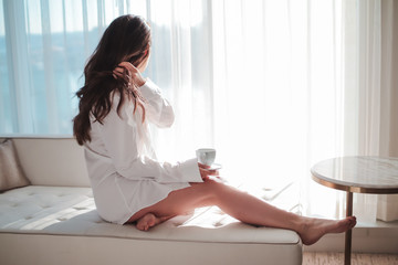young woman in dress shirt, enjoying coffee near a window