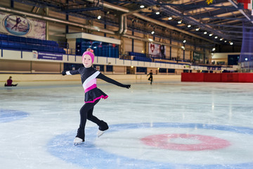 Full length portrait of little girl figure skating in indoor rink and looking at camera , copy space