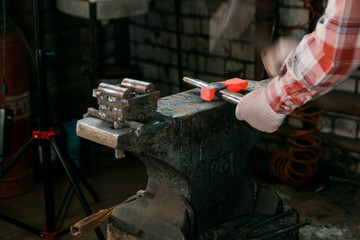 Blacksmith working with red hot metal workpiece of new axe on the anvil at the forge. Focus on anvil