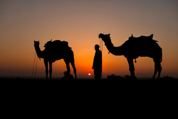 Fototapeta na wymiar Silhouette of camel trader crossing the Thar Desert in Jaisalmer, India.